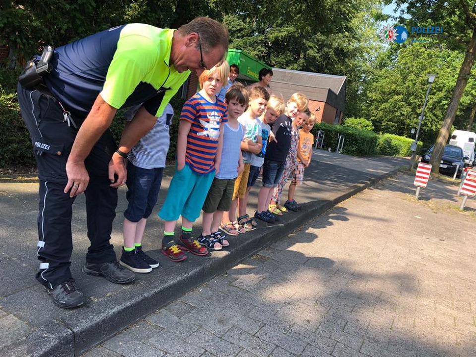 Polizist steht mit Kindern an der Borsteinkante 