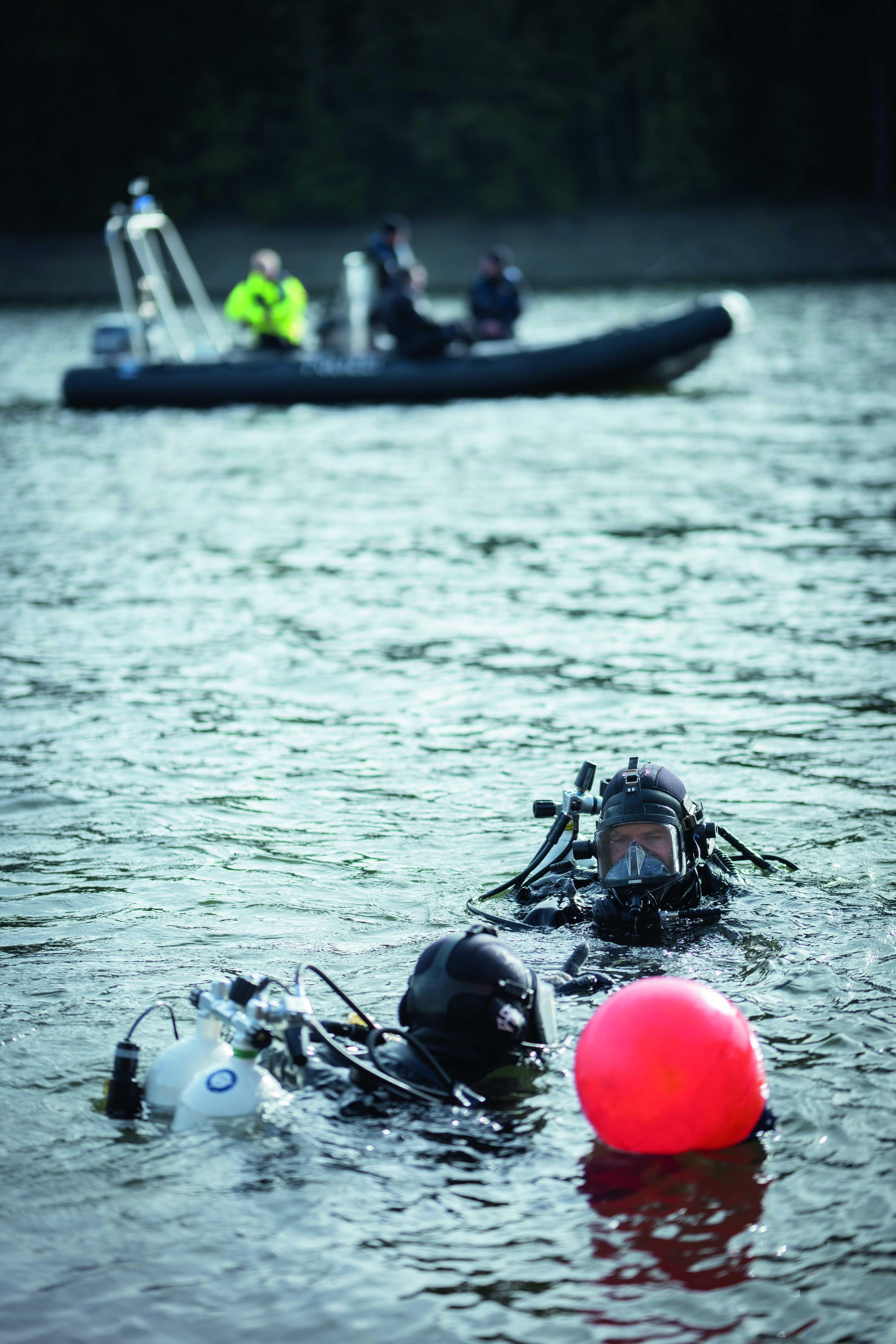 Zwei Taucher und ein Polizeiboot im Wasser, ein Fundort wird mit einer Boje markiert.