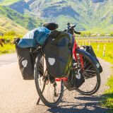 Fahrrad mit Gepäck auf einer Straße vor einem Bergpanorama