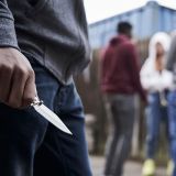 Links Messer in Nahaufnahme in der Hand einer unbekannten Person, im Hintergrund eine Gruppe unscharf dargestellt von drei Personen