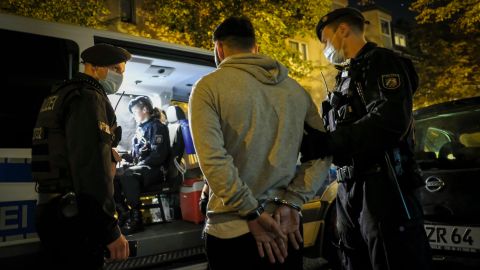 A person with a warrant for his arrest is taken away from a café.