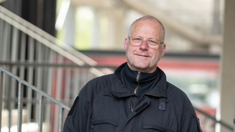 Hauptkommissar Kurt H. steht im RheinEnergieSTADION auf einer Treppe und lehnt sich ans Geländer. Er trägt schwarze Dienstkleidung.