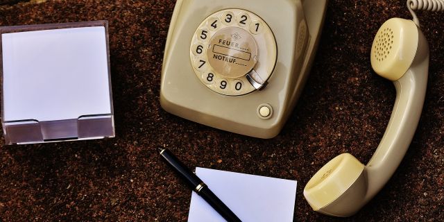 An old dial telephone with a piece of paper and pen next to it